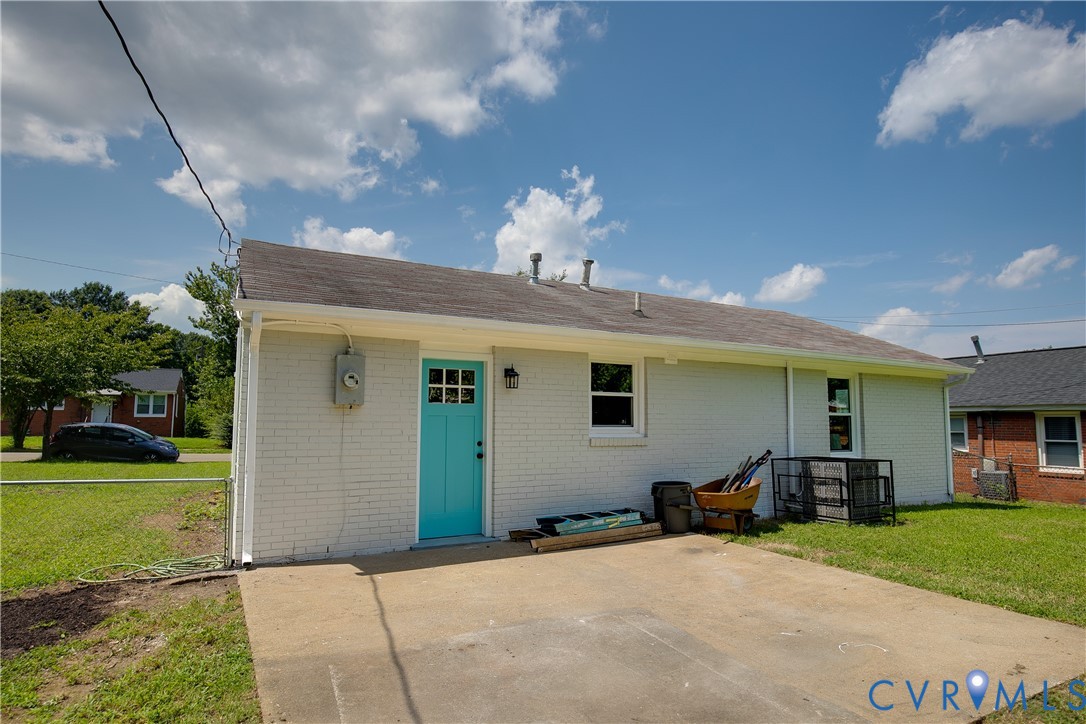 Exterior view featuring a white painted brick facade, a concrete patio, and a bold-colored paneled entry door