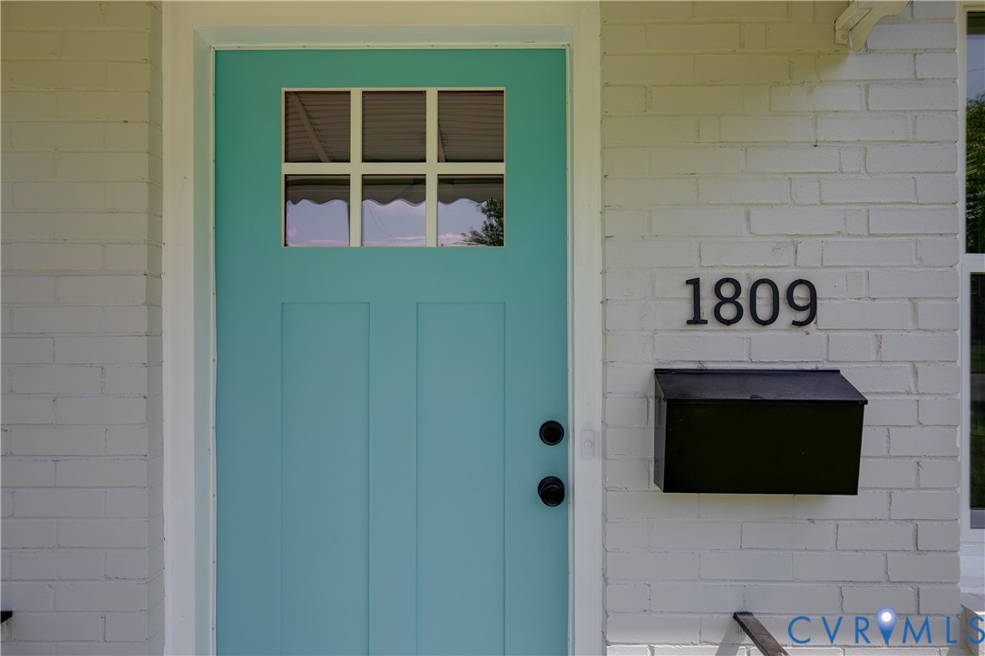 White painted brick exterior featuring a teal-colored entry door with a six-pane window insert, black matte hardware, and a matching black wall-mounted mailbox