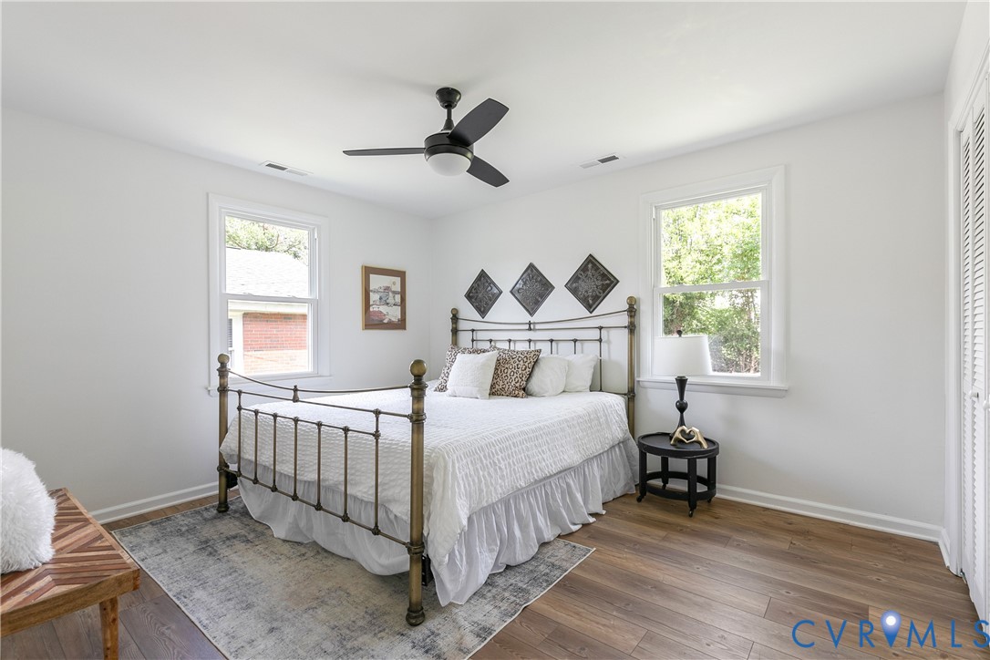 Room with wood-finish flooring, dual windows with white trim, matte black ceiling fan with integrated lighting, and louvered closet doors