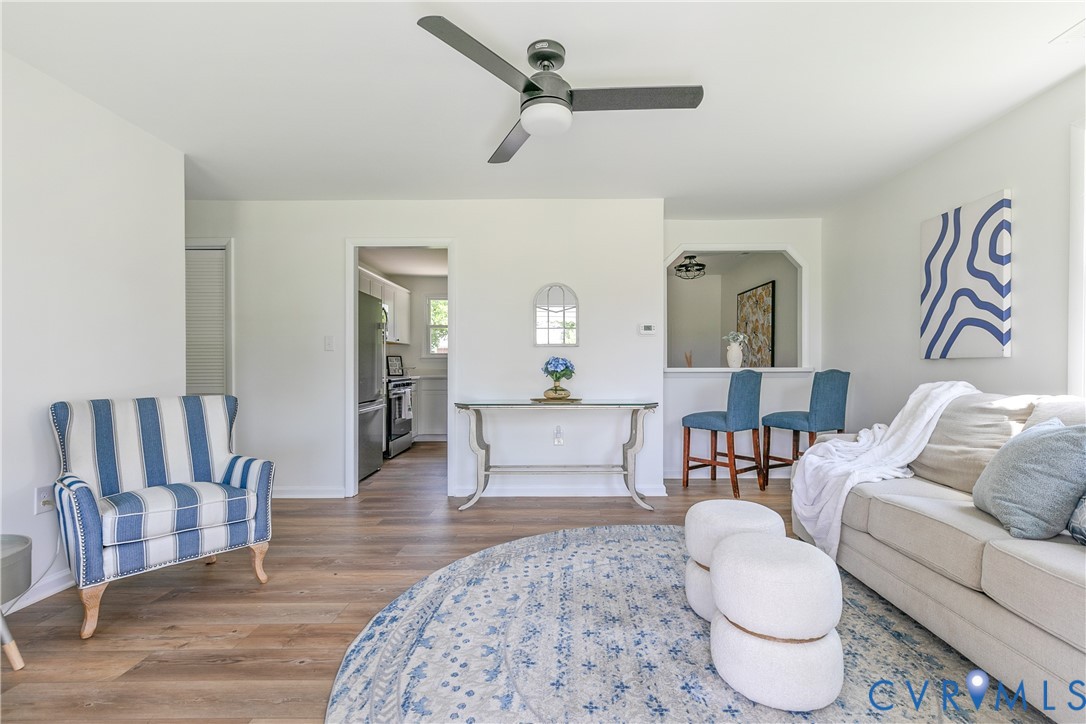 Living space featuring wood-finish flooring, a matte black three-blade ceiling fan with integrated lighting, and a pass-through opening to the kitchen
