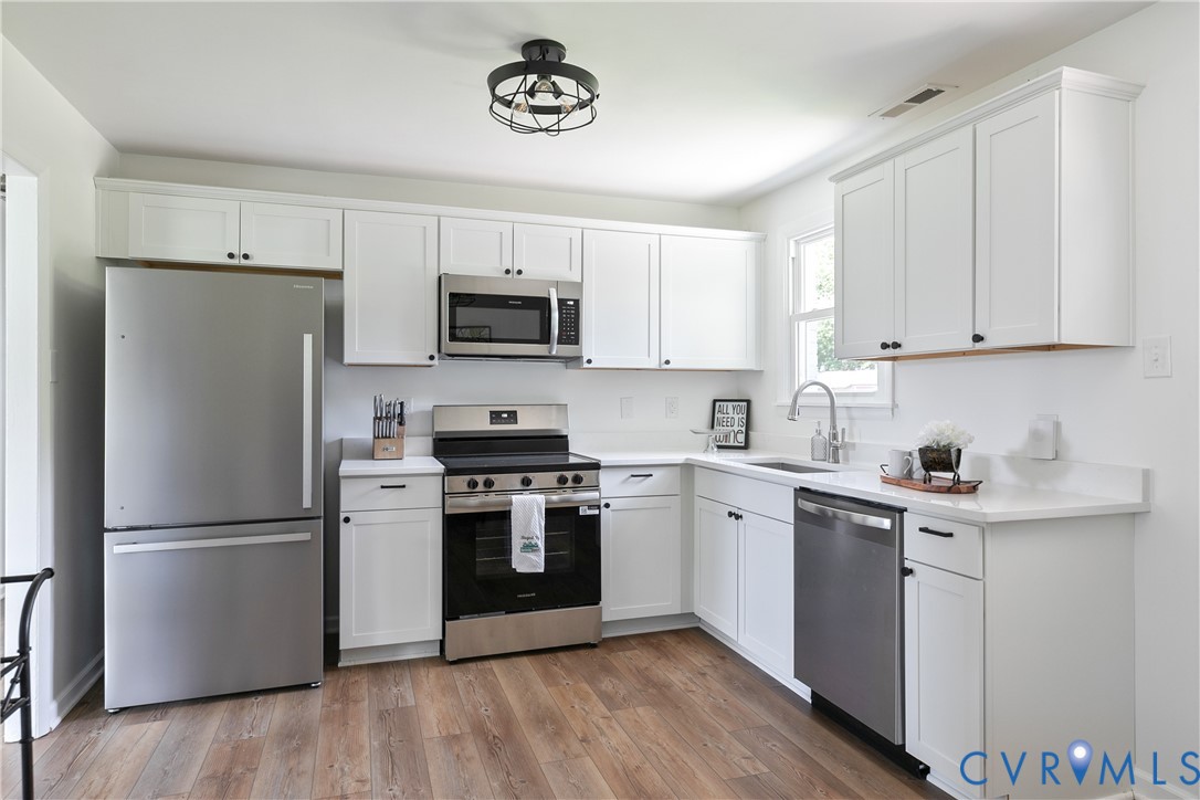 Kitchen featuring white shaker cabinetry, stainless steel appliances, solid surface countertops, a single-basin undermount sink with a gooseneck faucet, and wood-finish flooring