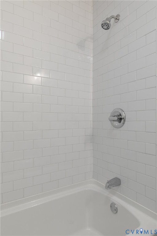 Full-height white subway tile surround with a polished chrome shower head, matching single-handle pressure balance valve, and standard porcelain tub