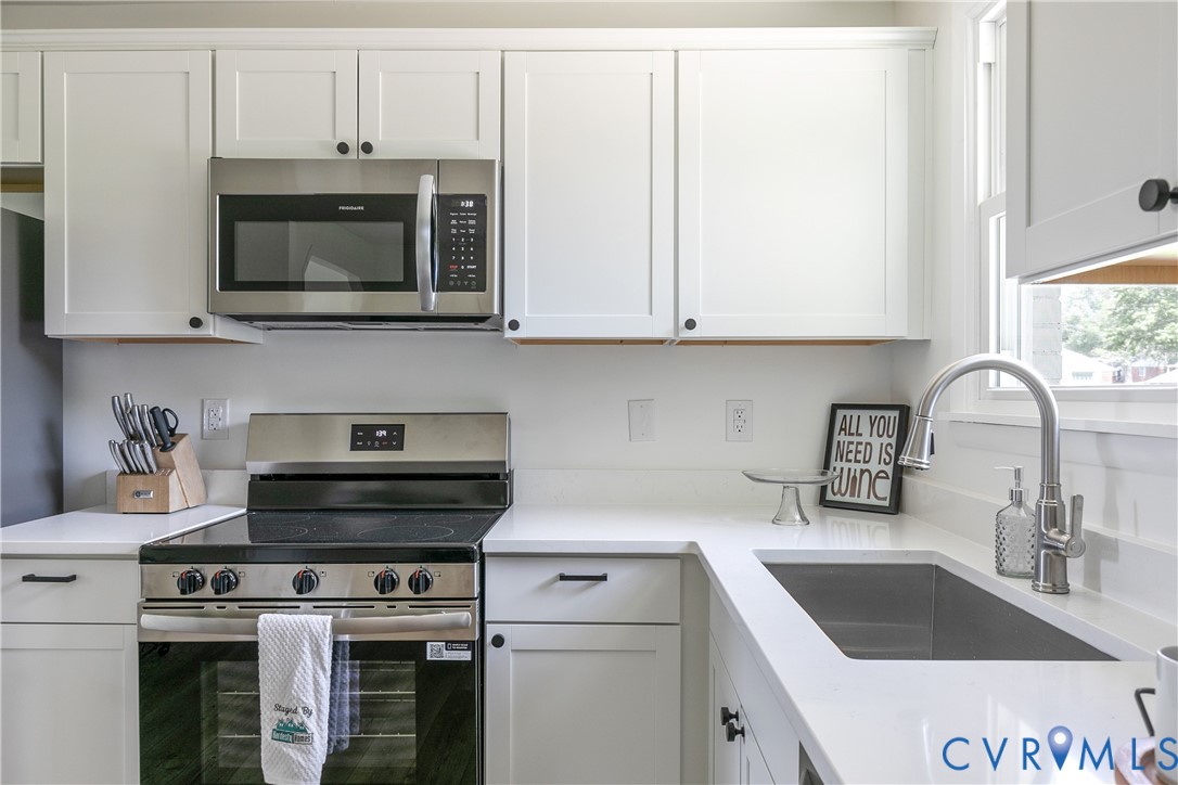 Kitchen featuring white shaker-style cabinetry, solid-surface countertops, stainless steel appliances, and an undermount sink with a gooseneck faucet