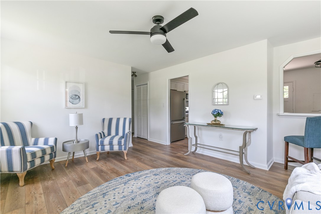 Living area featuring wood-finish flooring, a matte black ceiling fan with integrated lighting, and a partial wall opening