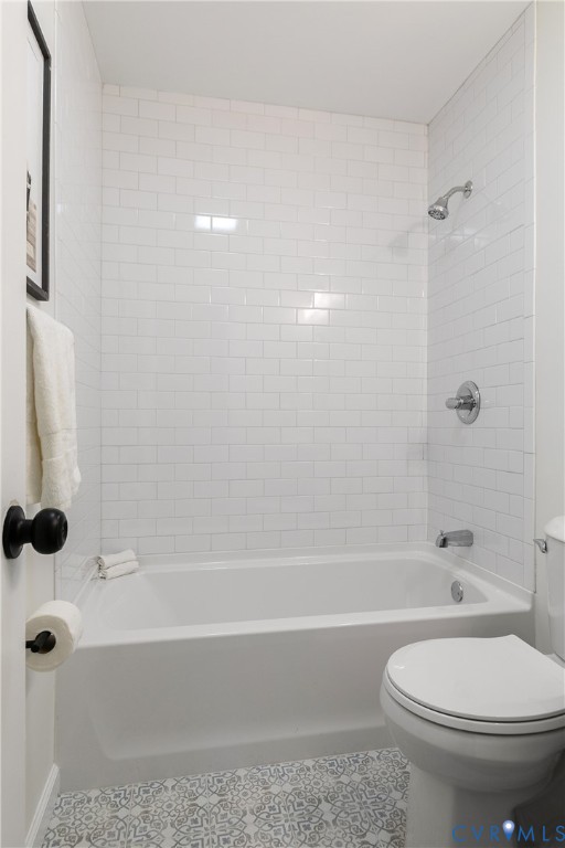 Full-height white subway tile surround, integrated soaking tub, polished chrome shower fixtures, and patterned decorative tile flooring