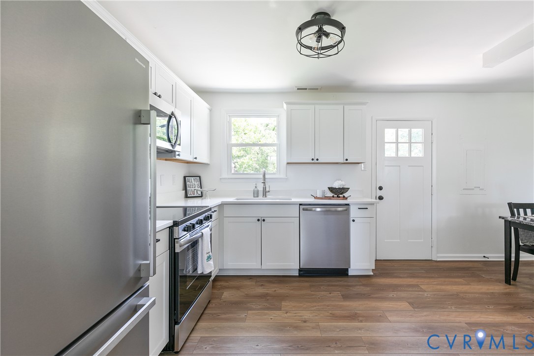 Kitchen featuring white shaker-style cabinetry, stainless steel appliances, wood-finish flooring, and a modern industrial-style ceiling fixture