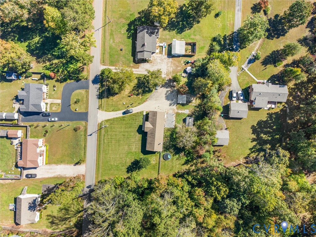 Aerial perspective featuring a spacious lot with extensive tree canopy coverage, expansive manicured lawn, and paved driveway access