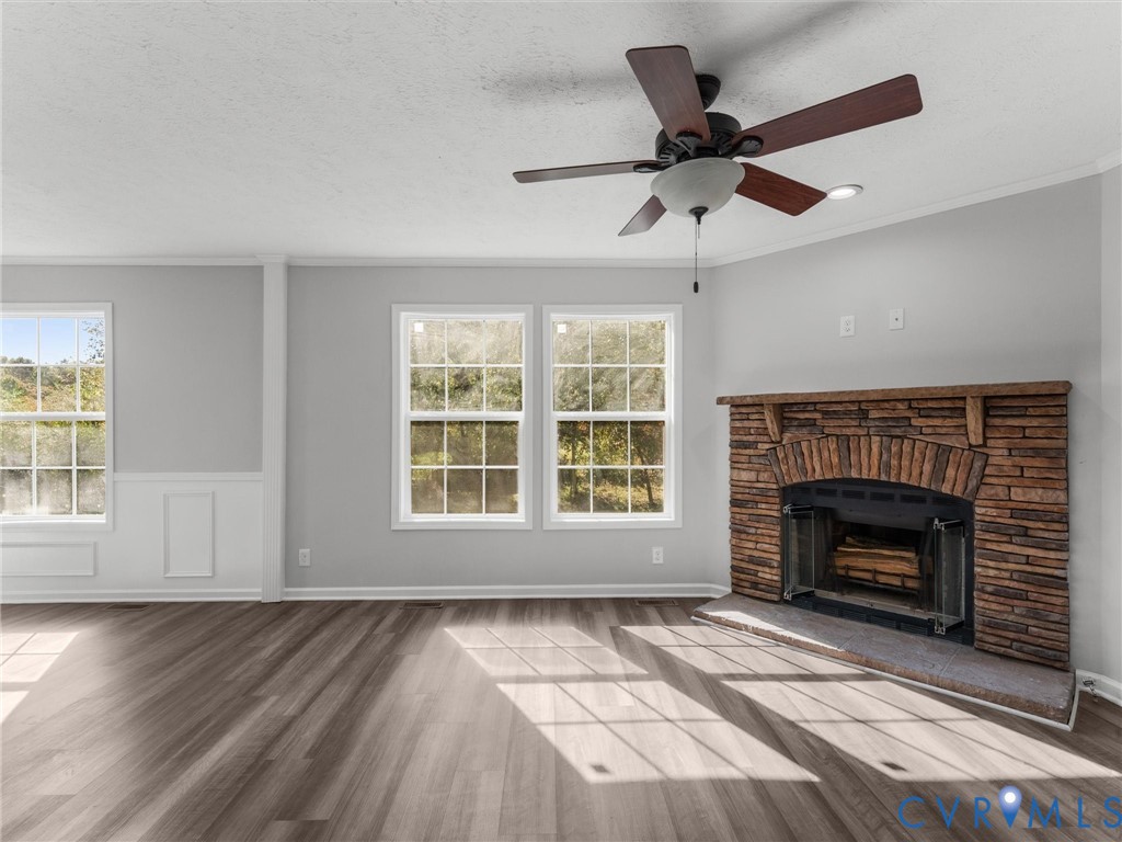 Stone-facade fireplace with a wooden mantel, wood-finish flooring, multi-pane windows, grid-pattern wall molding, and a ceiling fan with integrated lighting