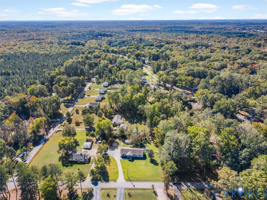 Aerial perspective of a multi-acre property featuring expansive grassy clearings, mature hardwood timber, and paved driveway access