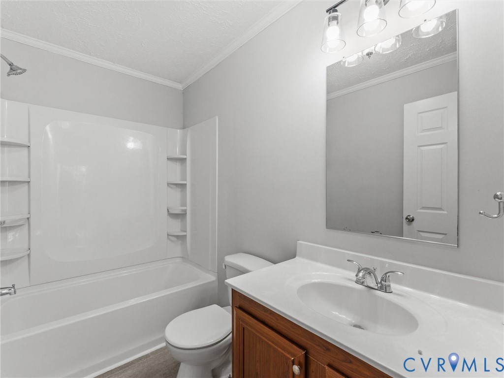 Bathroom featuring a wood-finish vanity with a composite countertop, integrated oval basin, polished chrome faucet, multi-light fixture, and a tub-shower combination with built-in shelving