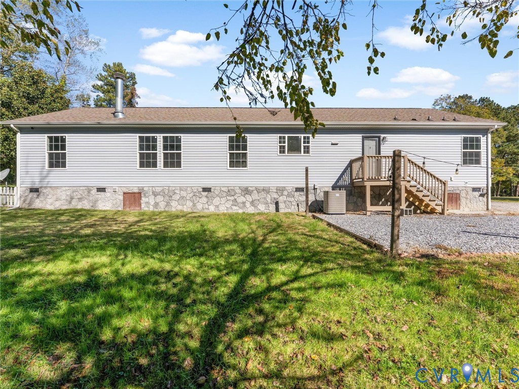 Exterior rear facade featuring horizontal siding, stone-patterned foundation veneer, elevated wooden deck, and gravel parking area