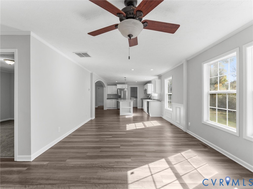 Open-concept interior featuring wood-finish flooring, a central ceiling fan with integrated lighting, paneled wainscoting, and an arched entryway