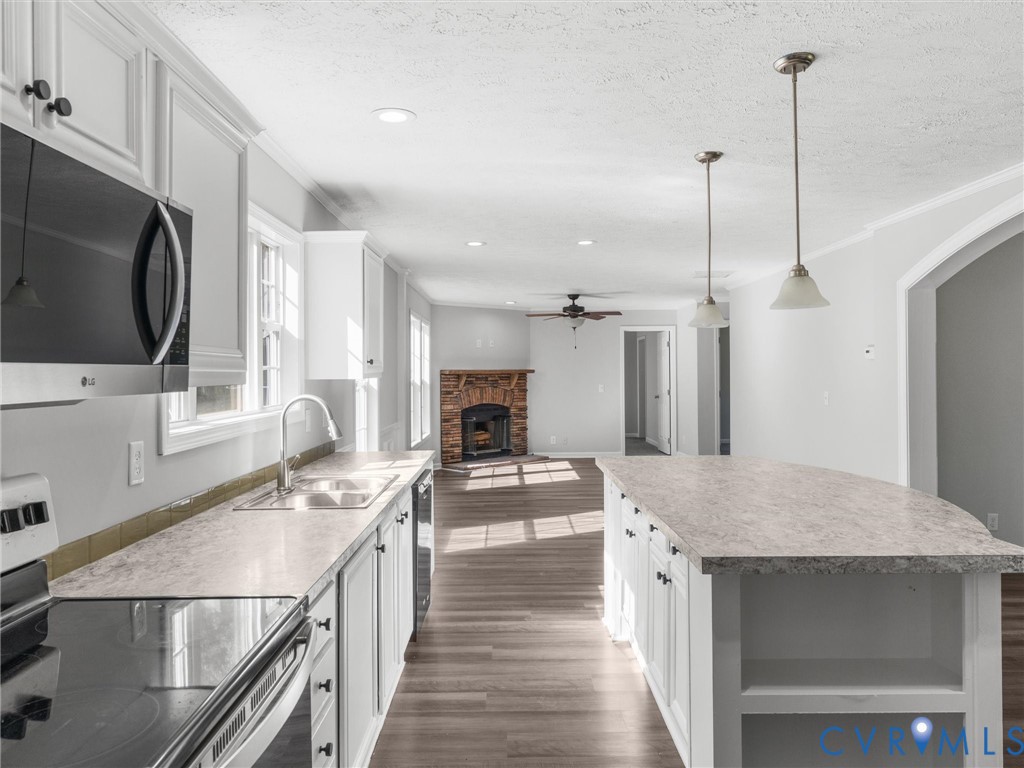 Kitchen featuring white cabinetry, stone-patterned countertops, a central island with built-in shelving, stainless steel appliances, and wood-finish flooring Kitchen featuring white cabinetry, stone-patterned countertops, a central island with built-in shelving, stainless steel appliances, and wood-finish flooring