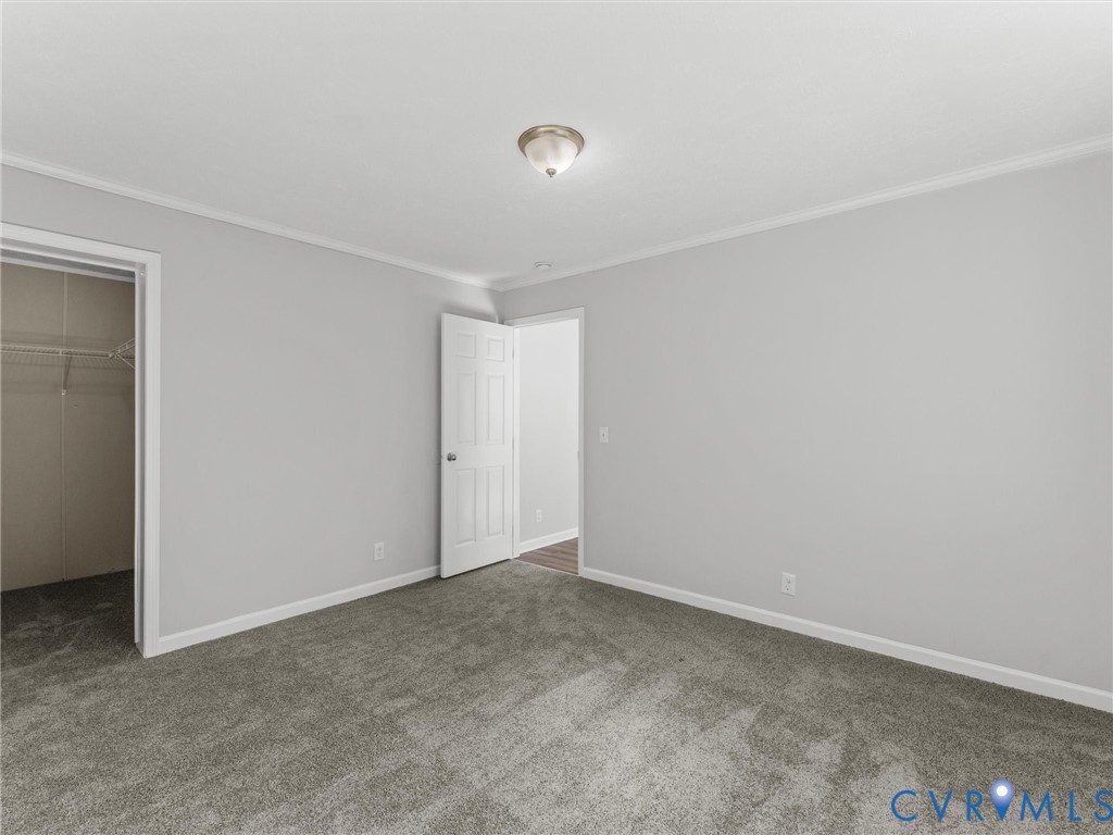 Neutral-toned interior space featuring plush carpeting, crown molding, a multi-panel interior door, and a flush-mount ceiling light fixture