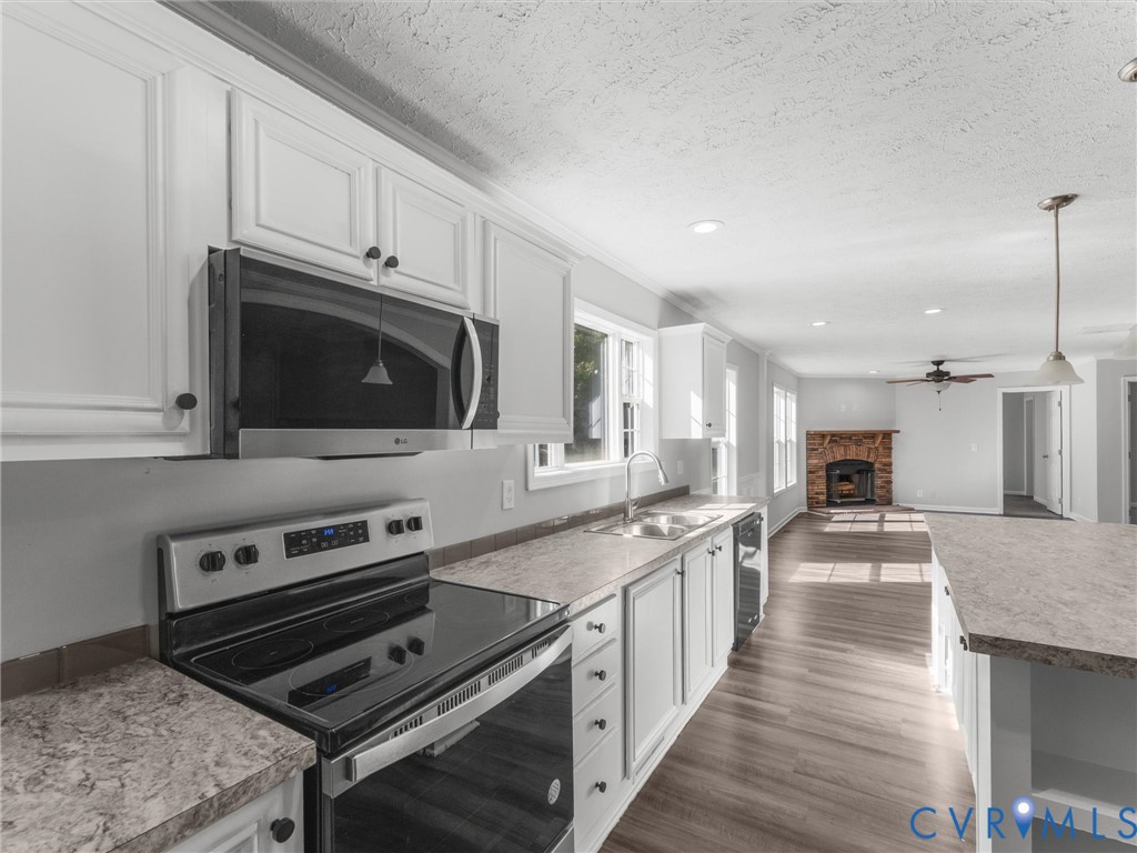 Kitchen featuring white cabinetry, stone-patterned laminate countertops, stainless steel appliances, wood-finish flooring, and a stone fireplace