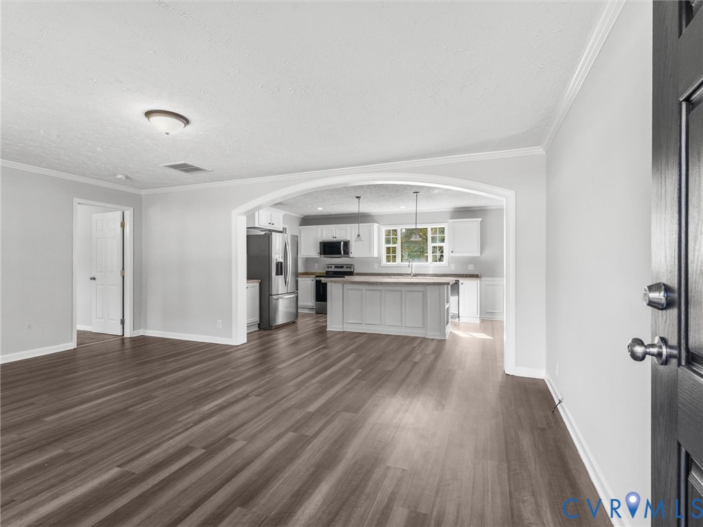 Open floor plan featuring a prominent architectural archway, wood-finish flooring, white cabinetry, a kitchen island, and stainless steel appliances Open floor plan featuring a prominent architectural archway, wood-finish flooring, white cabinetry, a kitchen island, and stainless steel appliances