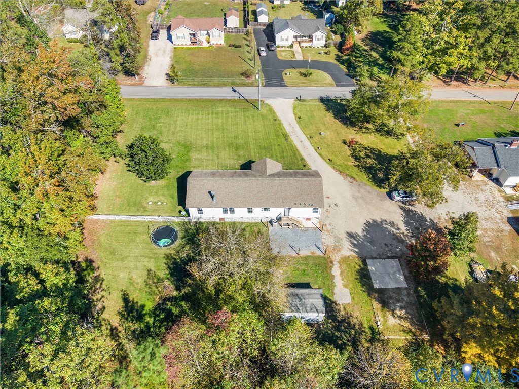 Aerial perspective of a detached residence featuring an expansive lawn, a multi-vehicle driveway, an attached deck, and mature perimeter trees