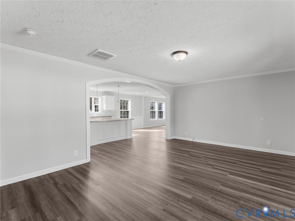 Interior space featuring wood-finish flooring, neutral wall paint, a large arched opening, and crown molding Interior space featuring wood-finish flooring, neutral wall paint, a large arched opening, and crown molding