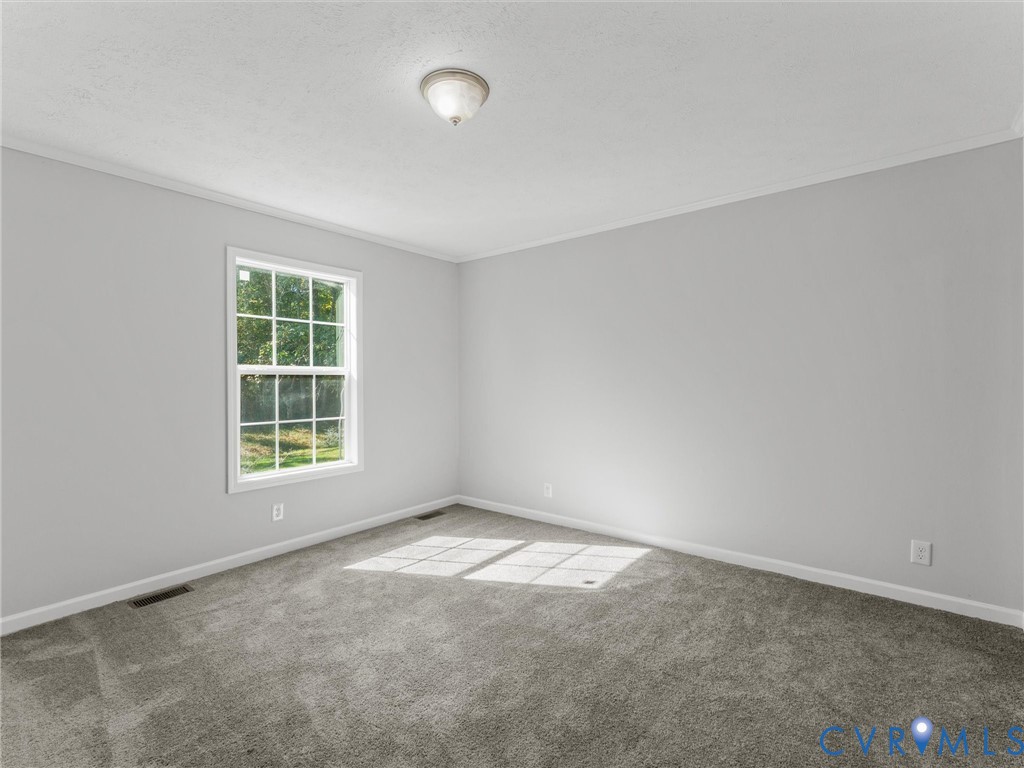 Neutral-toned interior space featuring neutral wall-to-wall carpeting, crisp off-white wall finishes, a single-hung window with a grid pattern, and a flush-mount ceiling light fixture