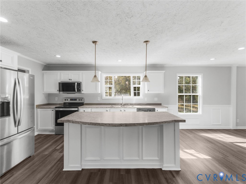 Kitchen featuring white cabinetry, center island with a stone-finish countertop, stainless steel appliances, pendant lighting, and wood-finish flooring Kitchen featuring white cabinetry, center island with a stone-finish countertop, stainless steel appliances, pendant lighting, and wood-finish flooring