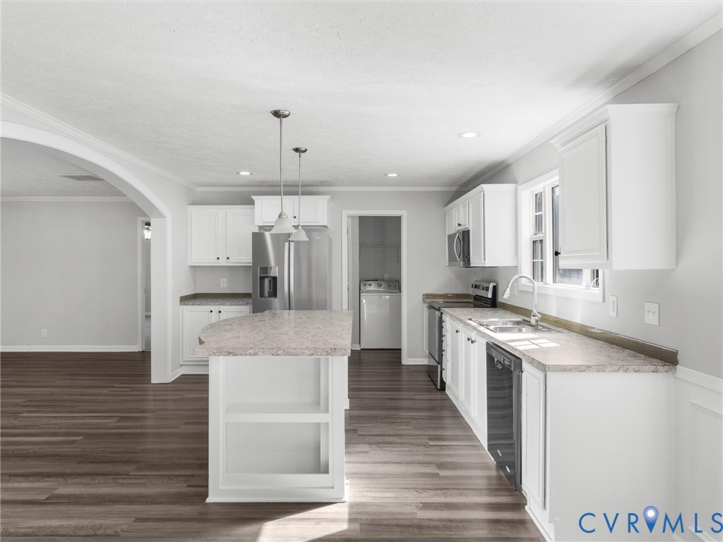 Kitchen featuring white shaker-style cabinetry, an expansive center island, wood-finish flooring, stainless steel appliances, and an arched architectural opening