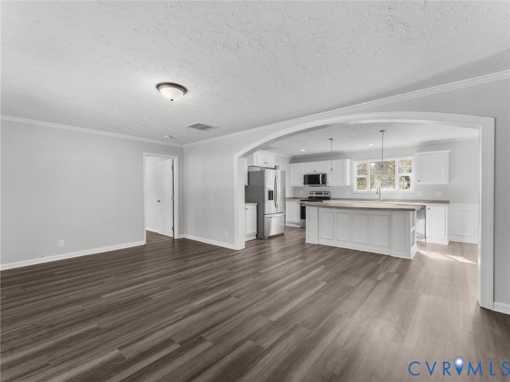 Open interior space featuring arched structural molding, wood-finish flooring, white cabinetry, center island with stone-finish countertop, and stainless steel kitchen appliances Open interior space featuring arched structural molding, wood-finish flooring, white cabinetry, center island with stone-finish countertop, and stainless steel kitchen appliances