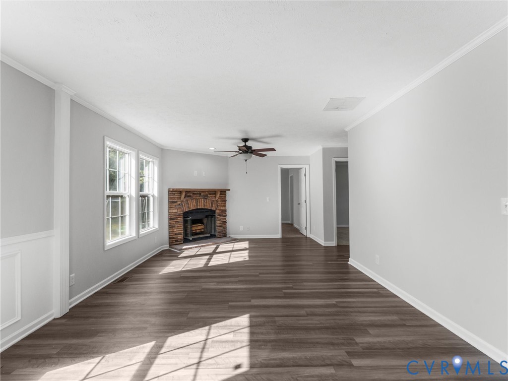 Interior space featuring wood-finish flooring, a corner fireplace with a stone-style facade, wainscoting, and a ceiling fan