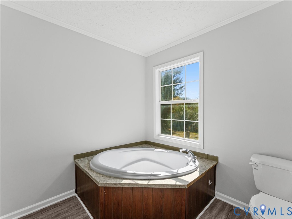 Corner soaking tub featuring a stone-finish deck, wood-toned cabinetry, polished chrome faucet, and window with natural light