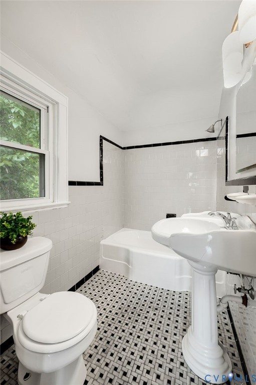 Bathroom featuring a porcelain pedestal sink, white subway tile wall surround with black accent trim, basketweave-pattern tile flooring, and a shower-tub combination