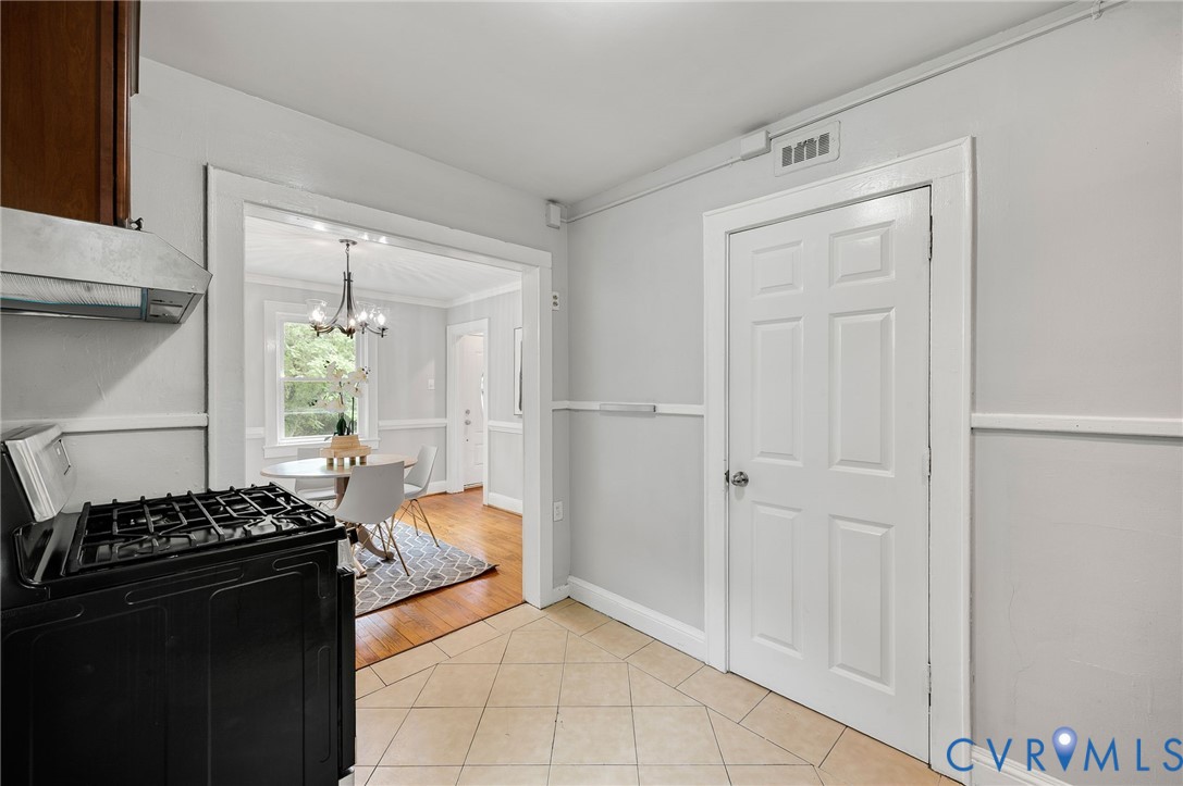 Kitchen featuring tile flooring, a six-panel door, and a stainless steel range hood, complemented by wainscoting and wood-finish flooring