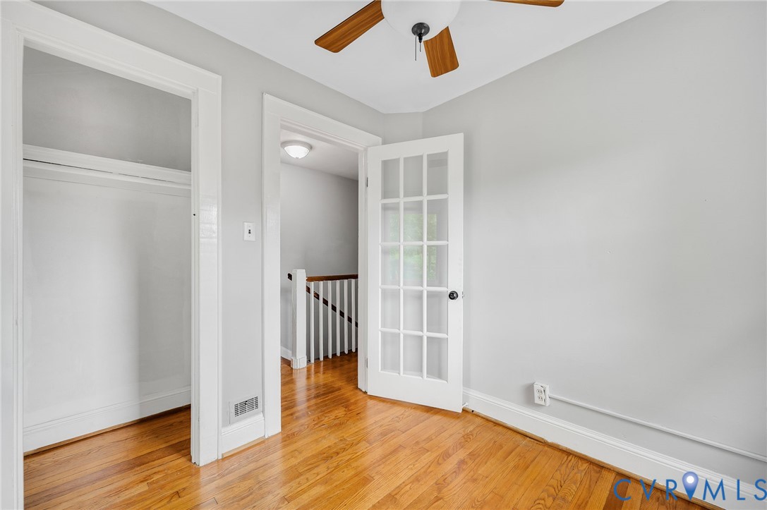 Wood-finish flooring, glass-paneled French door, ceiling fan, and built-in closet storage