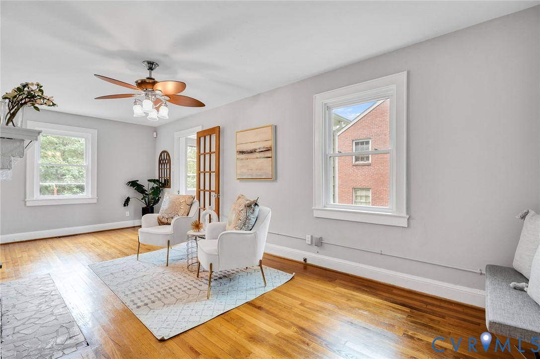 Living space featuring wood-finish flooring, double-hung windows with white trim, a multi-light wood door, and a ceiling fan with integrated lighting Living space featuring wood-finish flooring, double-hung windows with white trim, a multi-light wood door, and a ceiling fan with integrated lighting