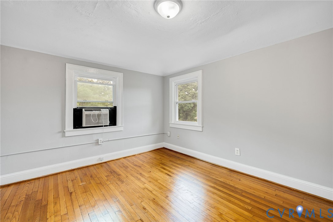 Interior room featuring wood-finish flooring, neutral wall tones, two double-hung windows, and a flush-mount ceiling light fixture
