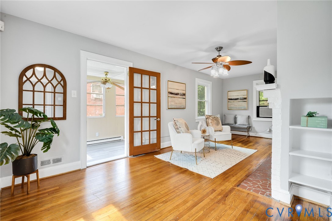 Hardwood flooring, wood-framed French door, built-in shelving, painted brick fireplace hearth, and ceiling fan with integrated lighting Hardwood flooring, wood-framed French door, built-in shelving, painted brick fireplace hearth, and ceiling fan with integrated lighting