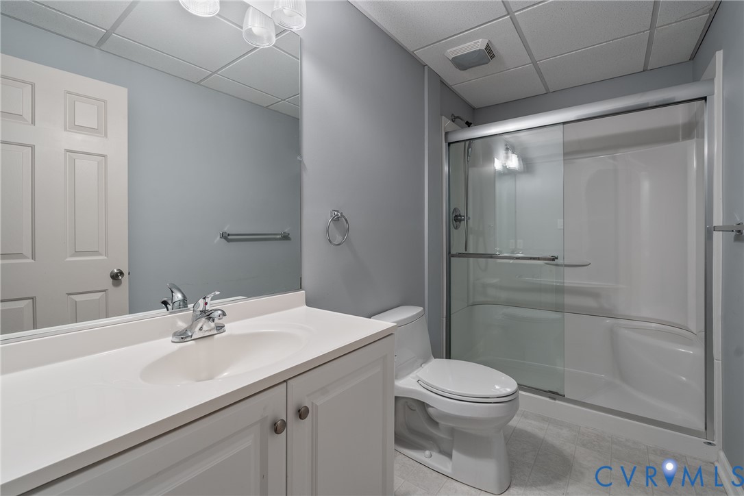 Bathroom featuring a white vanity with an integrated sink, a large wall-mounted mirror, a two-piece toilet, and a glass-enclosed shower with a built-in bench