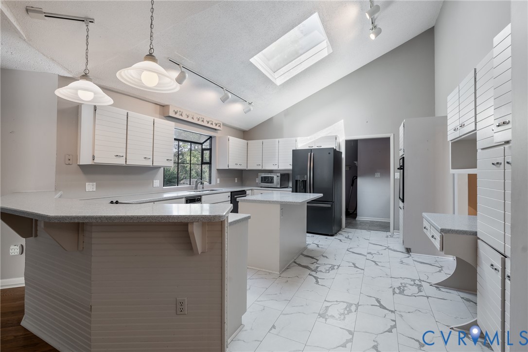 Kitchen featuring white paneled cabinetry, stone-finish countertops, a central island, a ceiling skylight, and track lighting
