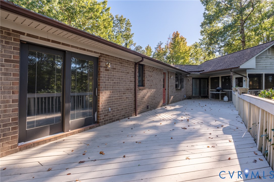 Expansive wood-finish deck with perimeter railings, brick exterior, and sliding glass entry doors