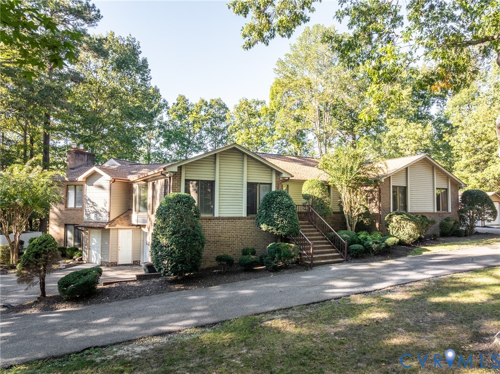 Multi-level exterior featuring a brick and siding facade, an elevated staircase with metal railing, an attached garage, and an asphalt driveway