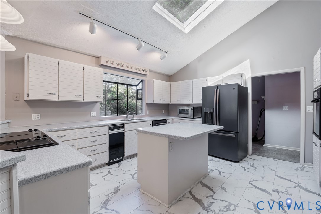 Kitchen featuring vaulted ceilings, a skylight, stone-finish countertops, a central island, and tile flooring