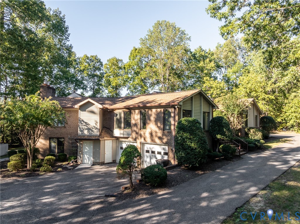 Multi-level exterior featuring a brick and siding facade, asphalt-paved driveway, integrated two-car garage, and established perimeter landscaping