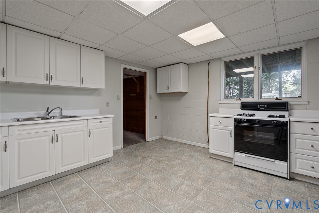 Kitchen featuring white cabinetry, built-in range, dual-basin stainless steel sink, tile flooring, and drop ceiling
