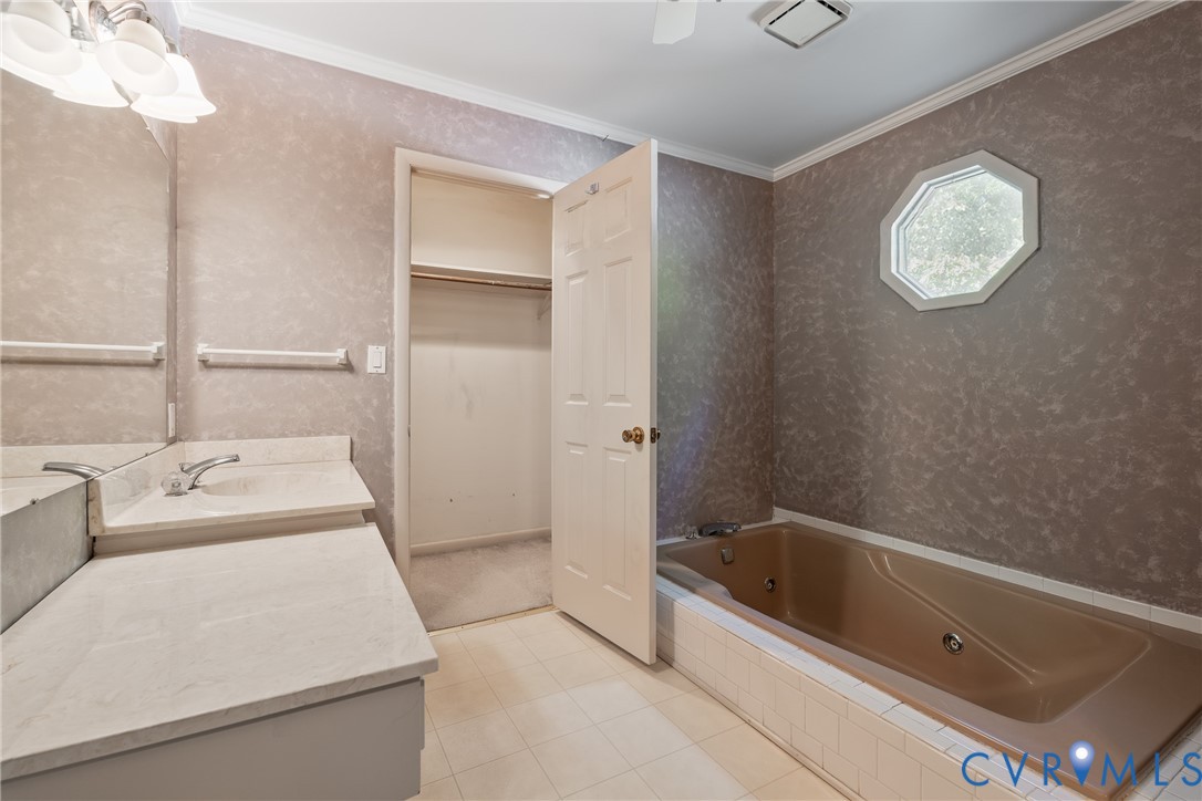 Bathroom featuring a jetted soaking tub with tiled surround, octagonal window, vanity with stone-finish countertop, and walk-in closet