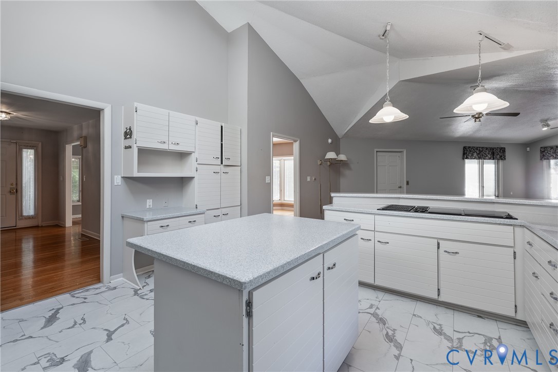 Kitchen featuring a vaulted ceiling, stone-patterned tile flooring, white cabinetry, a center island with a solid surface countertop, and dual pendant light fixtures