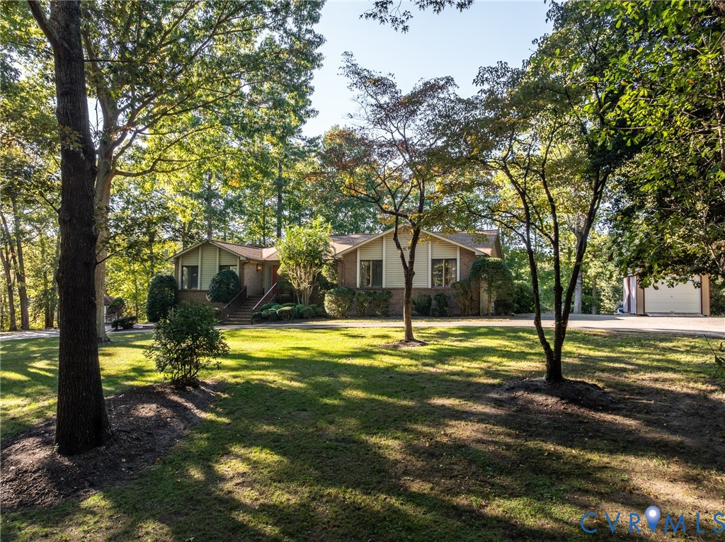 Exterior featuring a brick and siding facade, covered front entryway, expansive front lawn, mature canopy trees, and a detached garage
