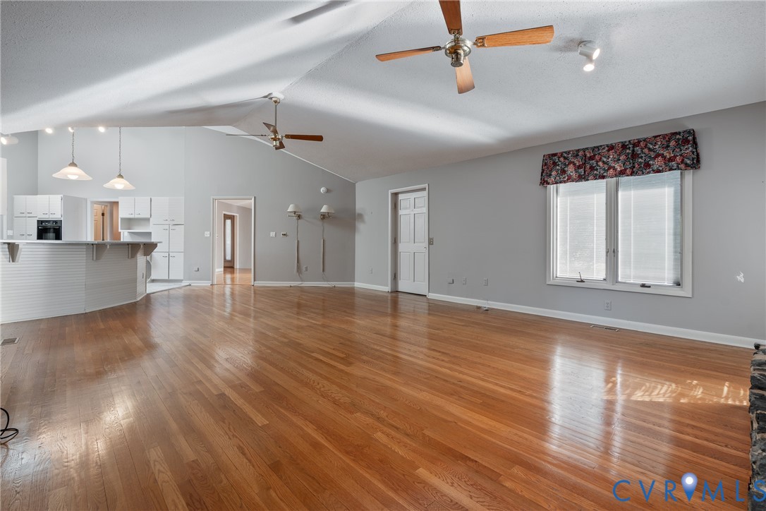 Vaulted ceilings with dual ceiling fans, expansive wood-finish flooring, and a wrap-around kitchen peninsula featuring white cabinetry