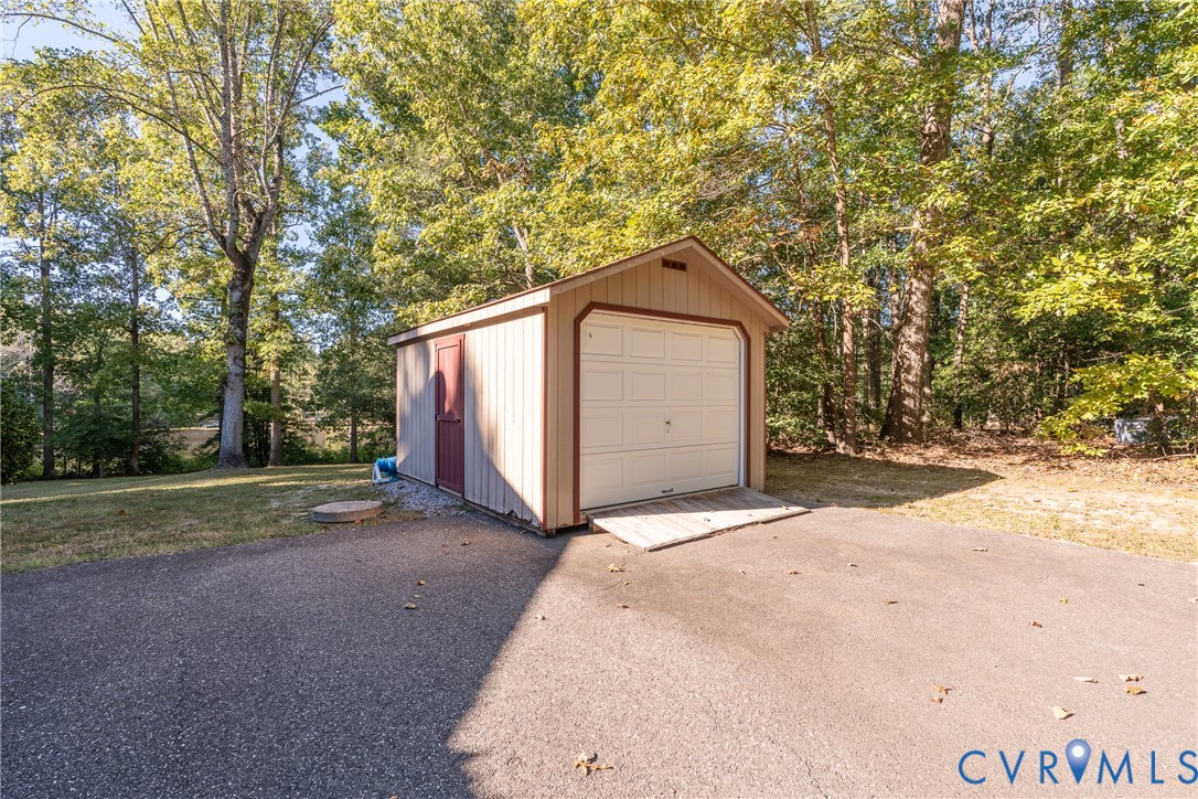 Detached shed with vertical siding, gable roof, roll-up garage door, side entry door, and paved access ramp