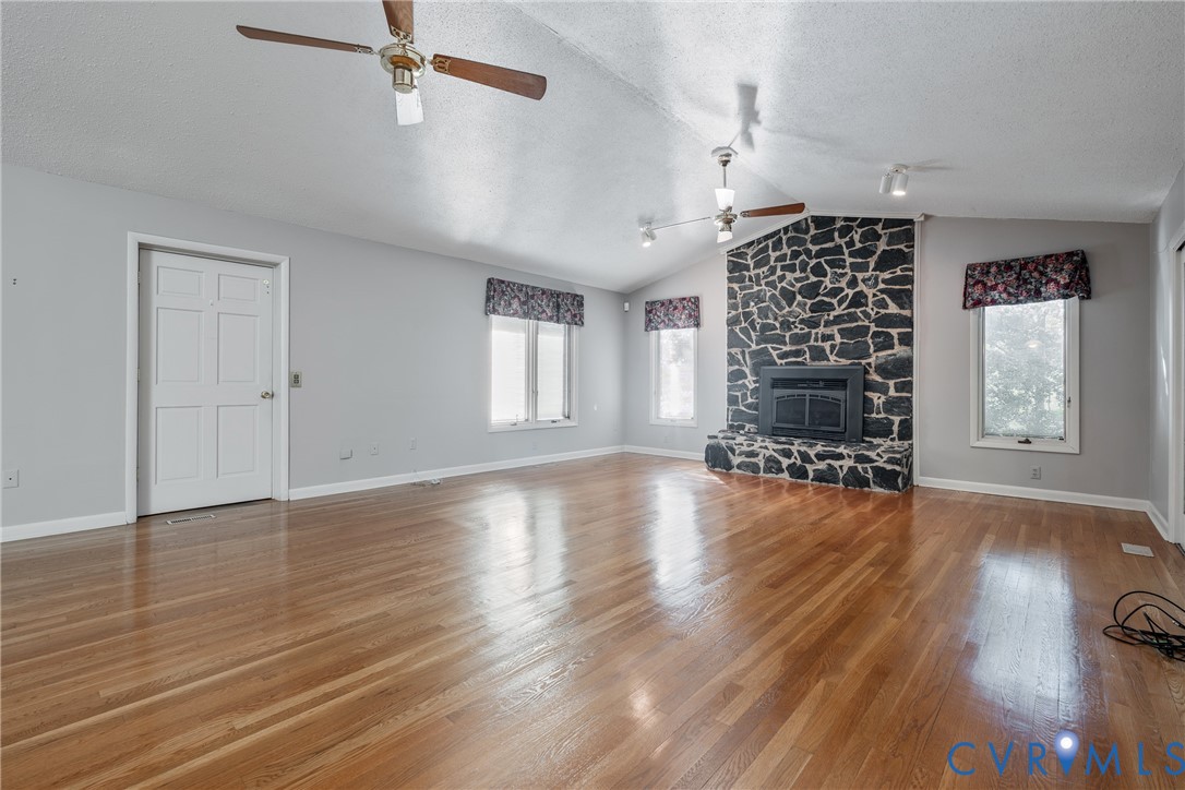 Vaulted ceilings with dual ceiling fans, wood-finish flooring, and a stone-clad floor-to-ceiling fireplace featuring a built-in firebox