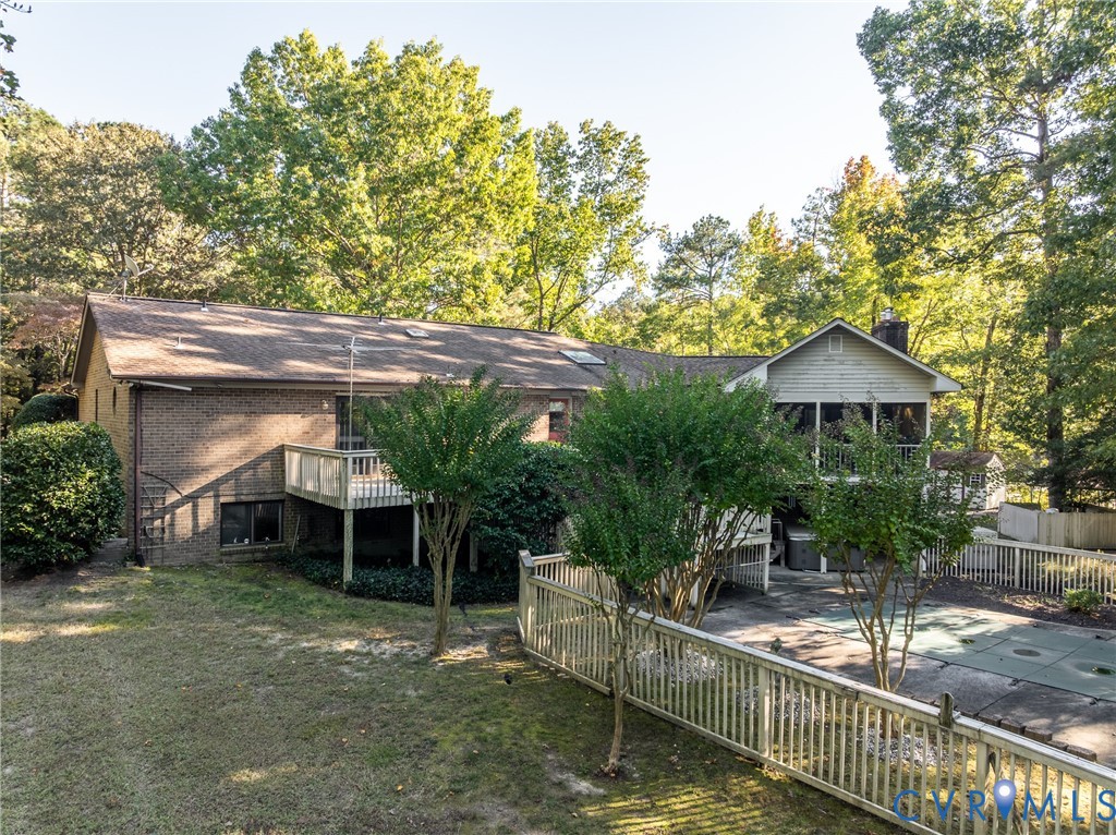 Brick exterior featuring a multi-level wooden deck, screened porch, fenced swimming pool area, and mature perimeter trees