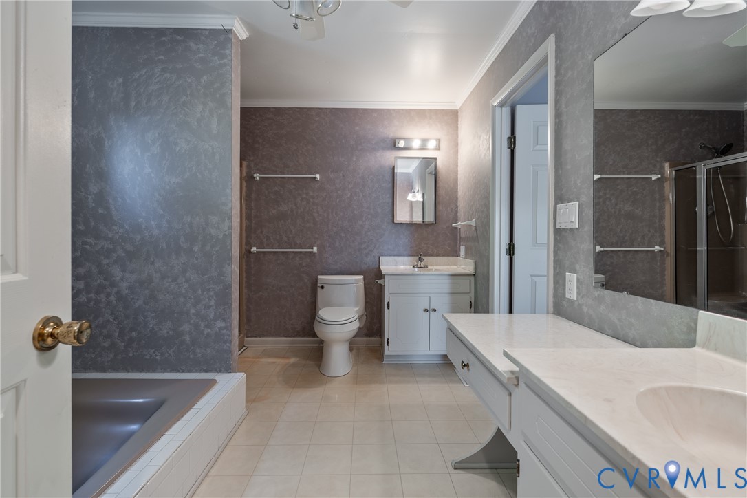 Bathroom featuring a built-in vanity with a solid-surface countertop, an integrated sink, an oversized wall-mounted mirror, and a tiled tub surround