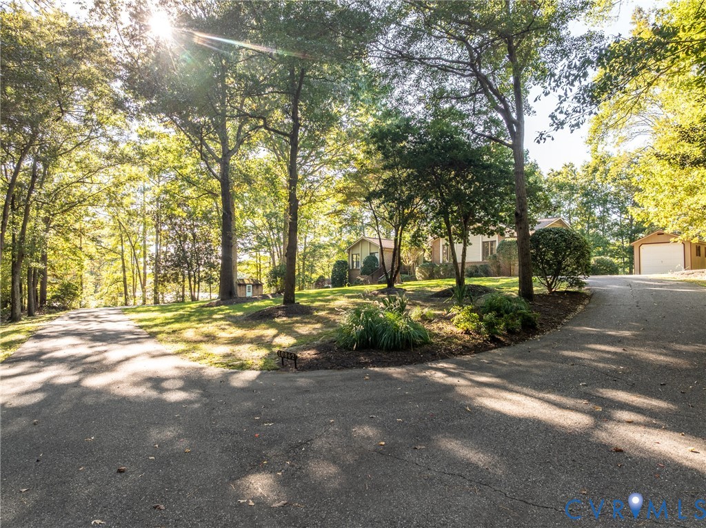 Asphalt driveway leading to a detached garage, expansive lawn, and mature canopy trees